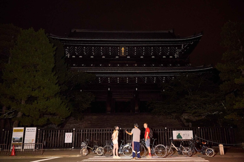 A traditional Japanese building at night with people and bicycles in front. 4