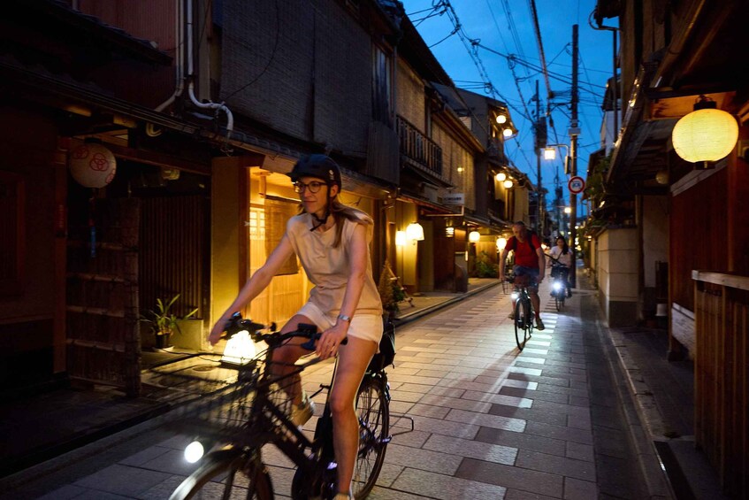 A person riding a bicycle down a narrow street at night. 1