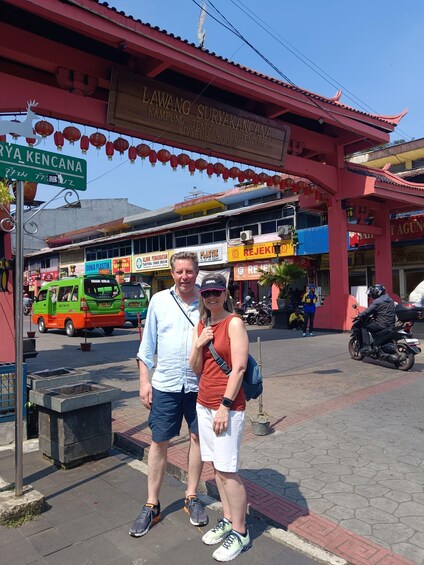 A couple standing in front of a traditional building with a sign that reads 'LAWANG-SURYAKANCANA.' 2