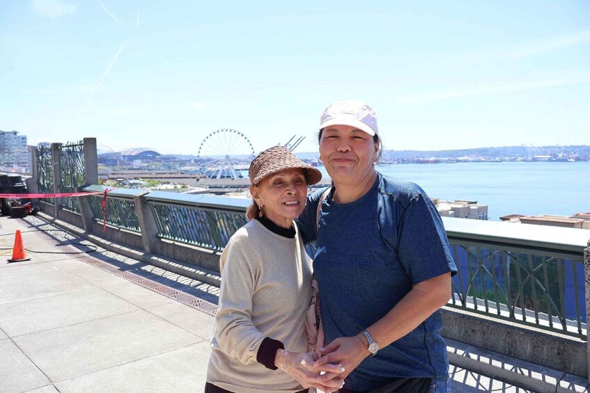 Two people standing on a bridge with a Ferris wheel and water in the background. 3