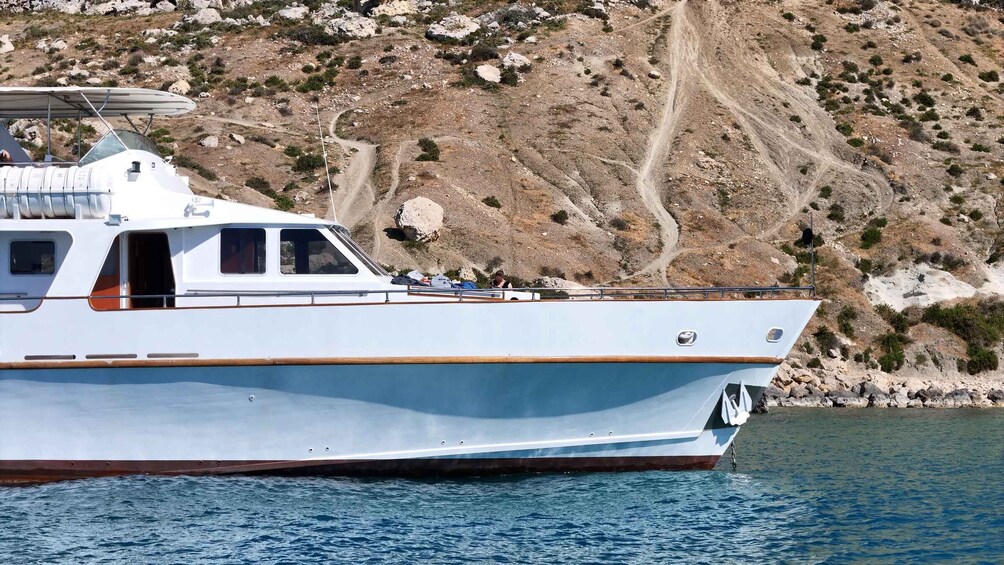 A white boat with a cabin and a cabin window, docked near a rocky coastline. 3