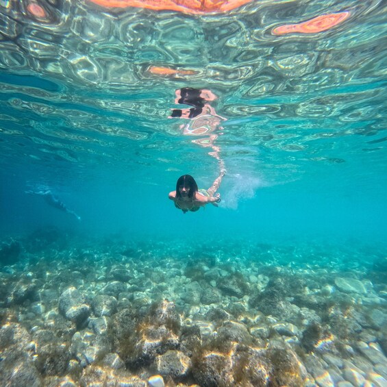 A person swimming underwater with a camera, surrounded by clear water and rocky seabed. 4