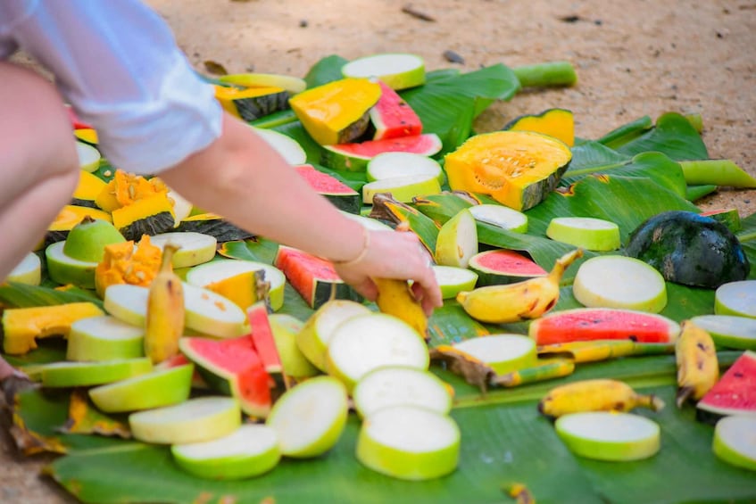 A person arranging sliced fruits on a banana leaf. 3