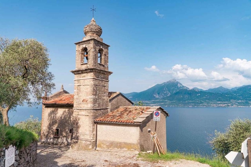 A church with a bell tower, a no parking sign, and a lake with mountains in the background. 1