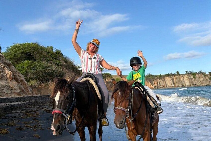 Two people riding horses on a beach with waves in the background. 3
