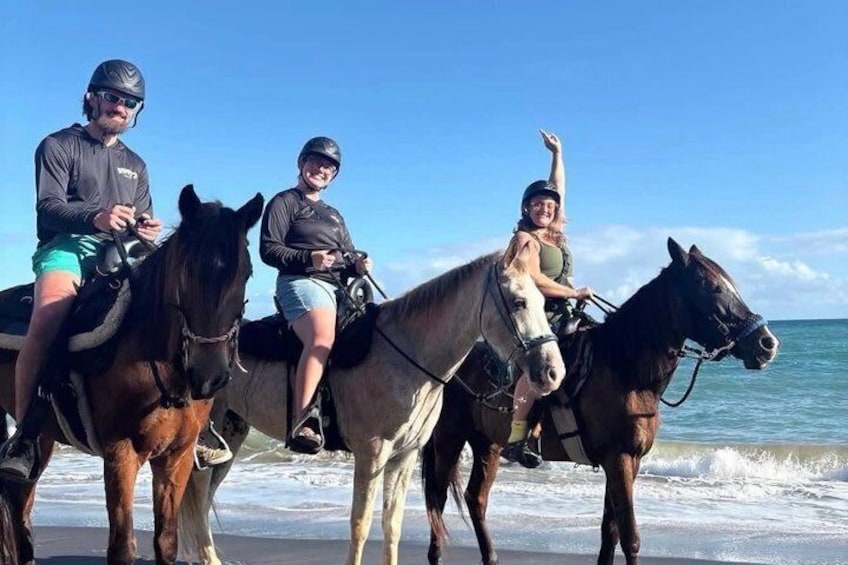 Three people riding horses on a beach with the ocean in the background. 4
