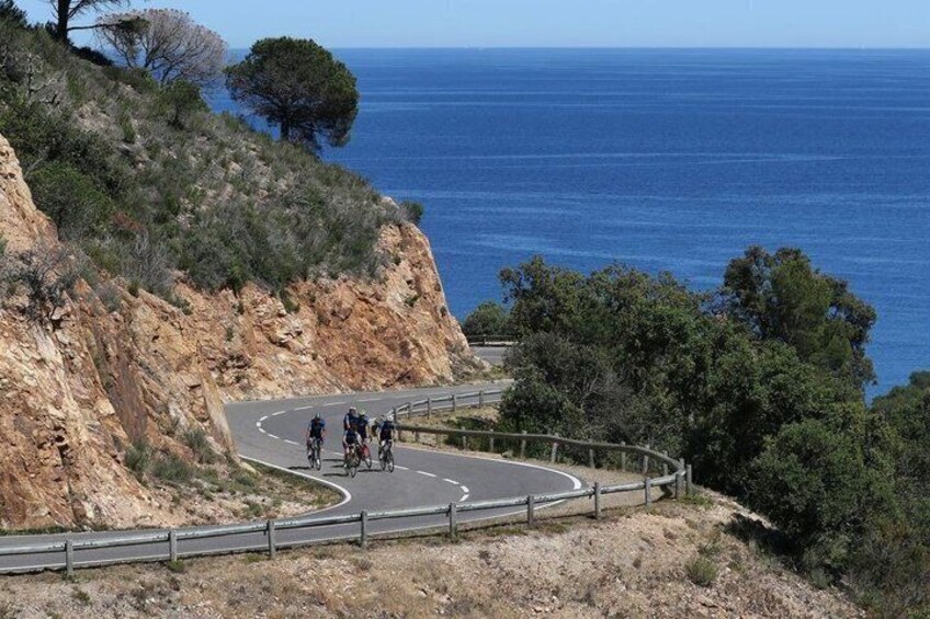 A winding coastal road with cyclists, a cliffside, and the ocean. 1