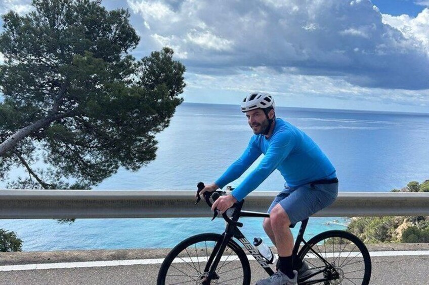 A person riding a bicycle on a road with a coastal view. 5