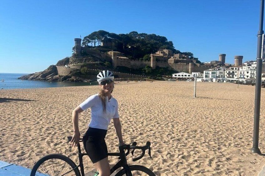 A person on a bicycle on a sandy beach with a historic fort in the background. 4