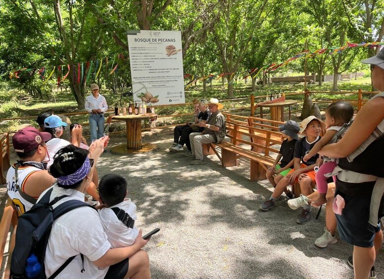 A group of people seated and standing outdoors, with a signboard in the background. 5