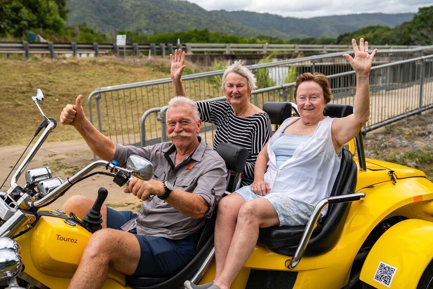 Three people on a yellow motorcycle with a scenic landscape in the background. 2