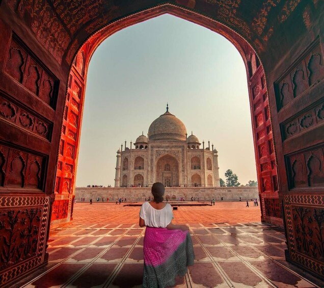 A person sitting in an ornate archway with the Taj Mahal in the background. 1