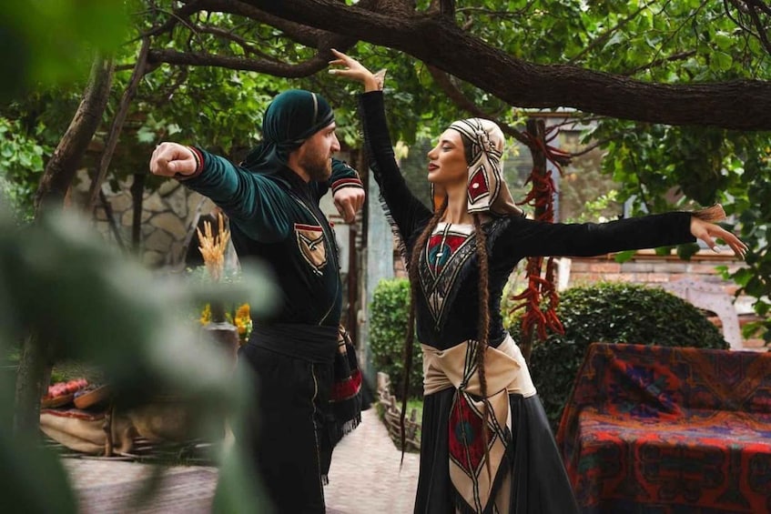 Two people in medieval costumes in a garden with a stone wall and a colorful couch. 2