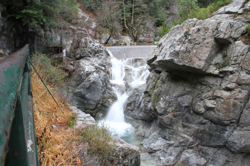 A waterfall cascading over rocks in a forested area with a bridge in the foreground. 2