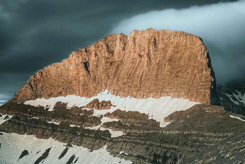 A mountain with a prominent peak and snow patches. 1