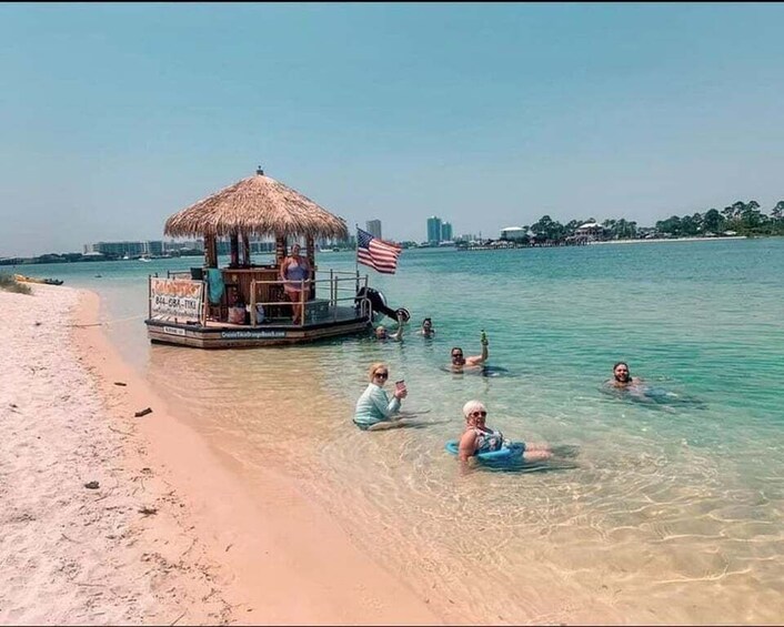 A beach with a thatched-roof boat, clear turquoise water, and people swimming. 5