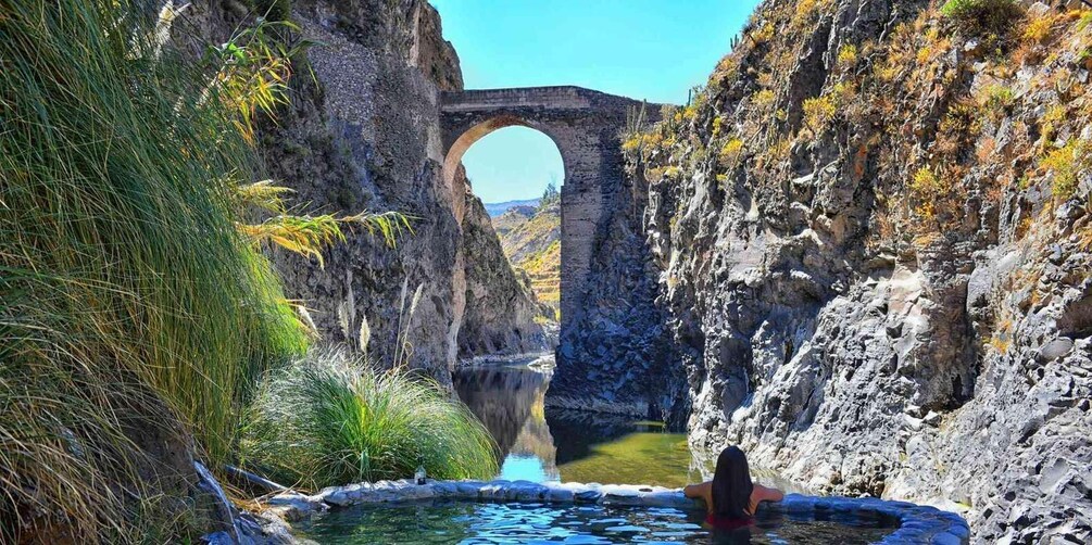 A natural pool with a stone arch bridge in the background. 5