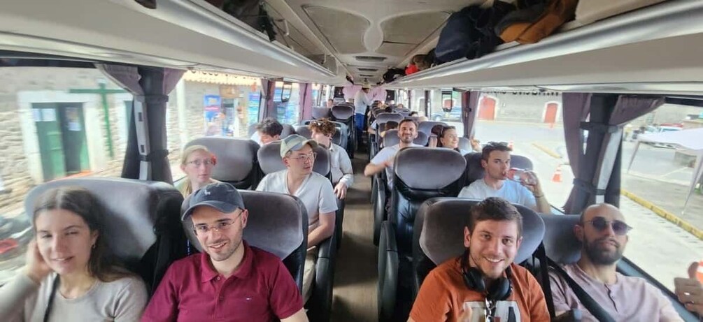 A bus interior with passengers seated, windows showing a building, and a road outside. 3