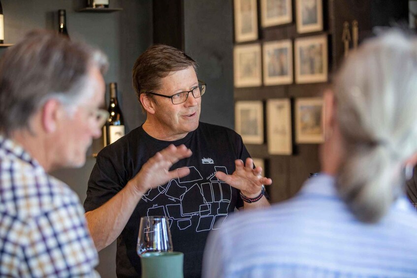 A person gesturing while speaking to others in a room with framed pictures on the wall. 5