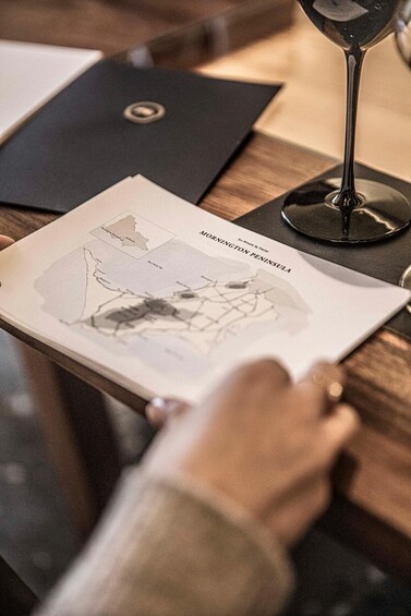 A person holding a map titled 'Mornington Peninsula' with a wine glass on the table. 1