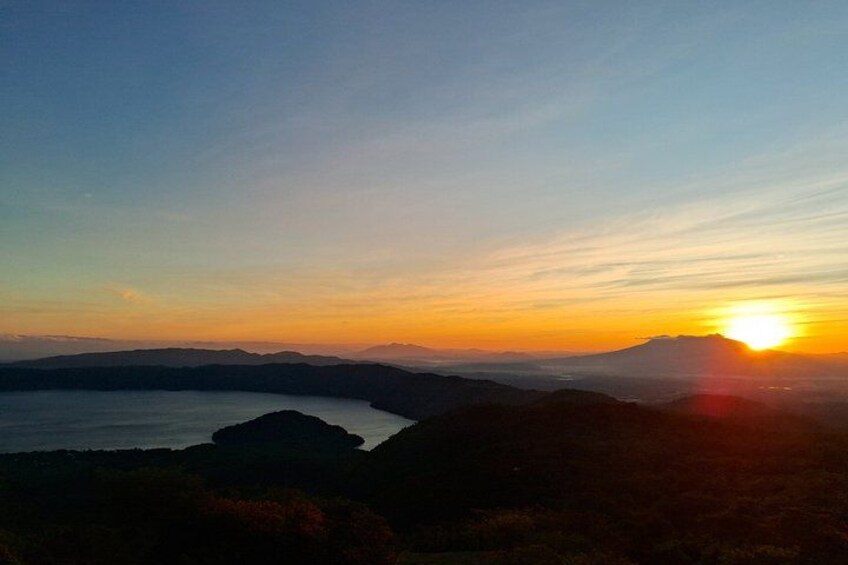 A sunset over a mountainous landscape with a body of water in the foreground. 1