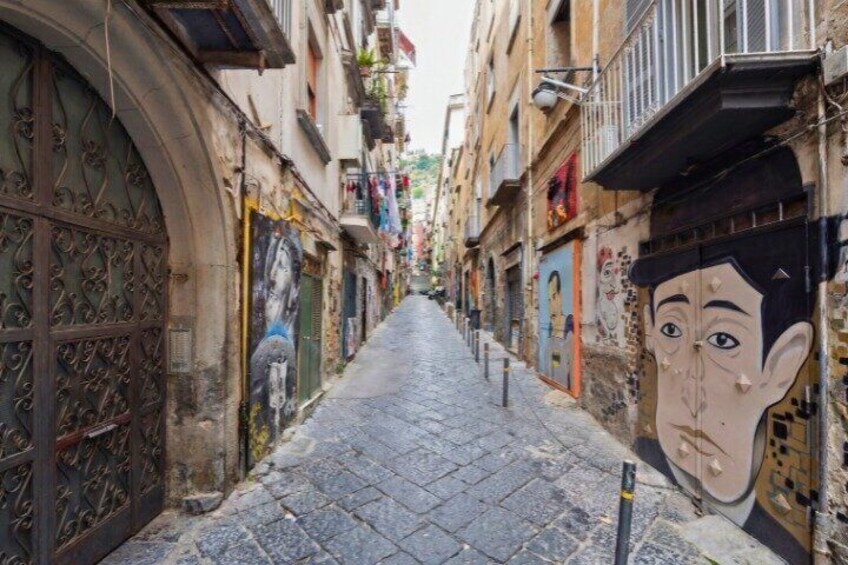 A narrow street with cobblestone pavement, ornate metal gates, and colorful murals on the buildings. 4