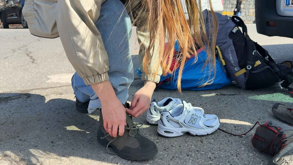 A person tying shoelaces on a road with a backpack and a car in the background. 5