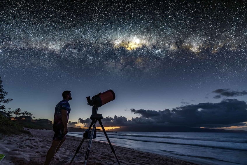 A person using a telescope on a beach at night, with stars and the Milky Way visible in the sky. 1