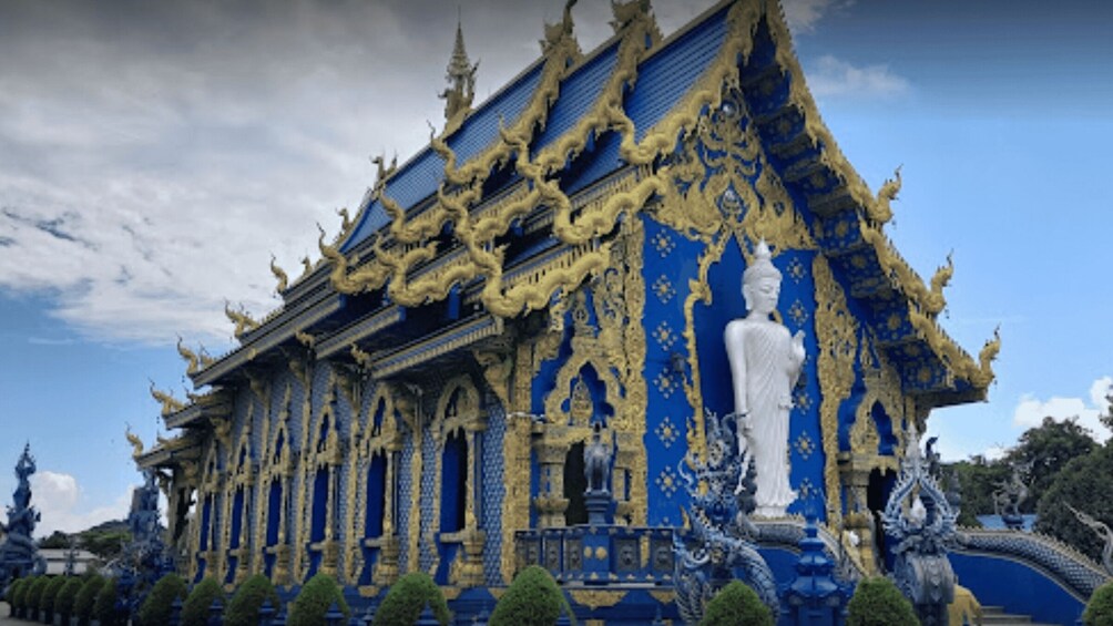 A temple with intricate blue and gold decorations, a large statue, and a traditional Thai roof. 3
