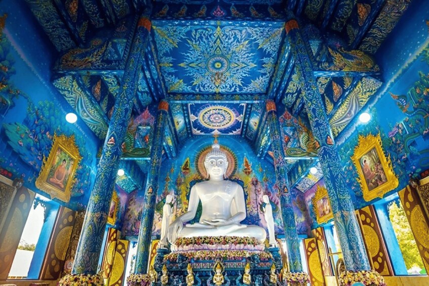 A large white Buddha statue in a richly decorated temple with intricate blue and gold patterns on the ceiling and walls. 2