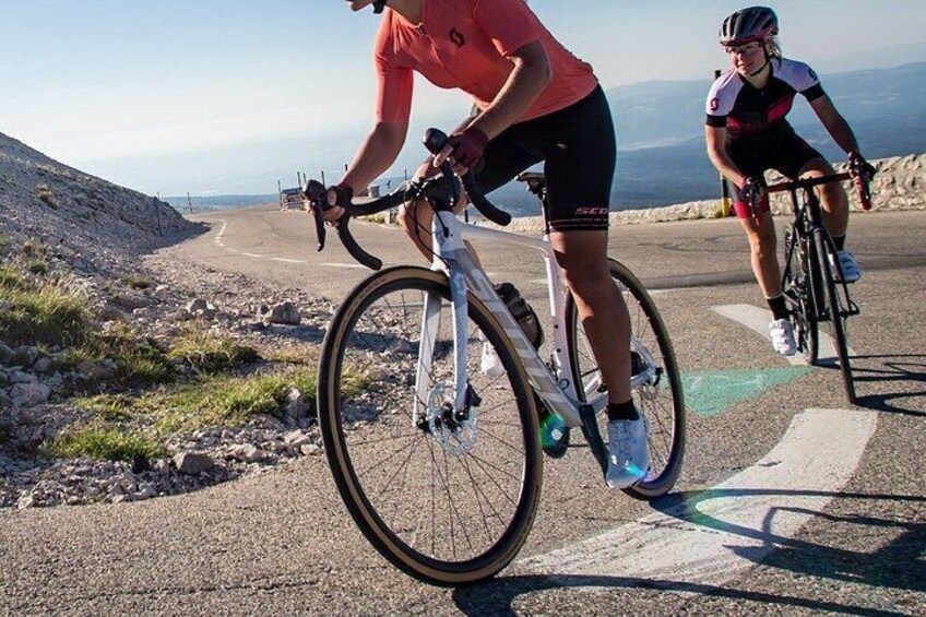Two cyclists on a paved road with a mountainous landscape in the background. 4