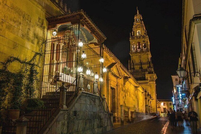 A historic street at night with a prominent clock tower, illuminated buildings, and cobblestone pavement. 2