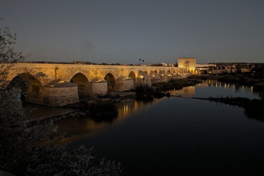 A stone bridge with arches over a calm river at dusk. 2