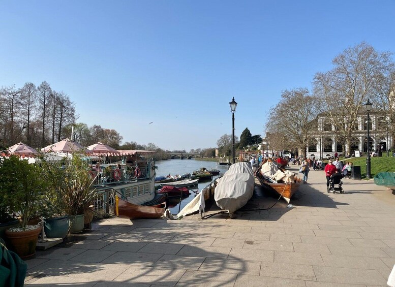A riverside walkway with boats, a covered area, and a historic building. 1