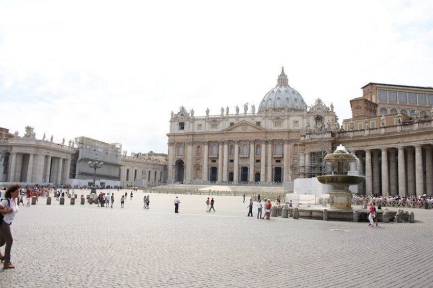 A large open square with a historic building featuring columns and a dome, surrounded by tourists. 2