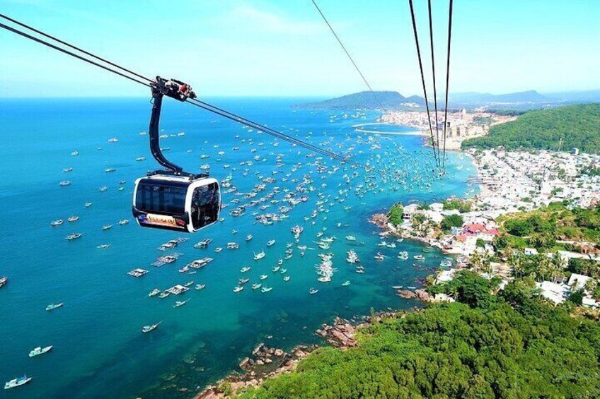 A cable car over a coastal town with boats in the water and greenery on the hills. 4