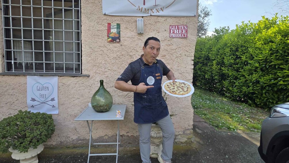 A person holding a gluten-free pizza outside a building with a sign indicating gluten-free products. 4