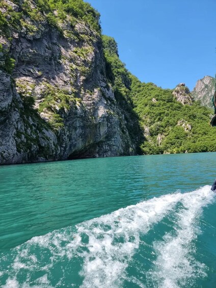 A boat moving through turquoise water with rocky cliffs and lush greenery in the background. 2