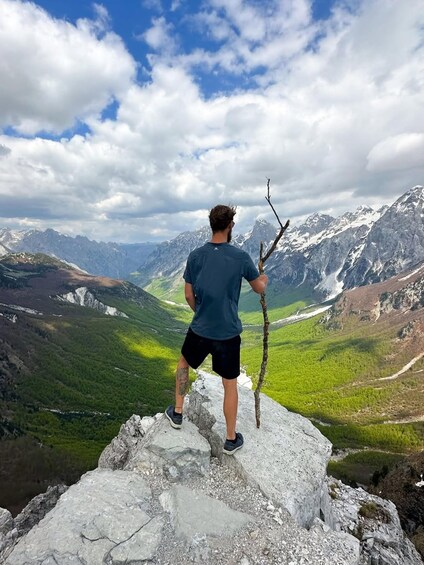 A person standing on a rocky outcrop with a view of a mountainous landscape. 1