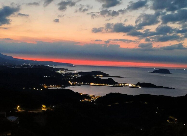 A coastal landscape at dusk with a sunset, illuminated city lights, and a prominent island in the distance. 3