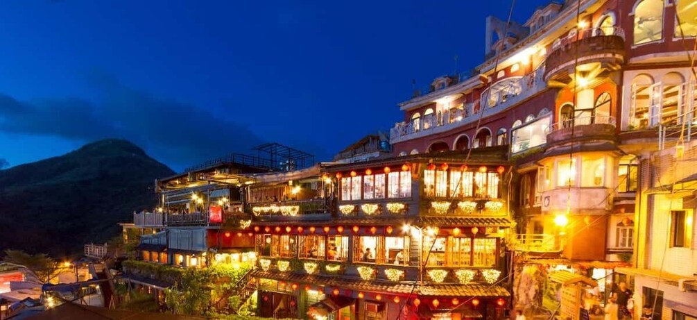A brightly lit multi-story building with balconies and traditional architectural features, likely a hotel or resort. 1