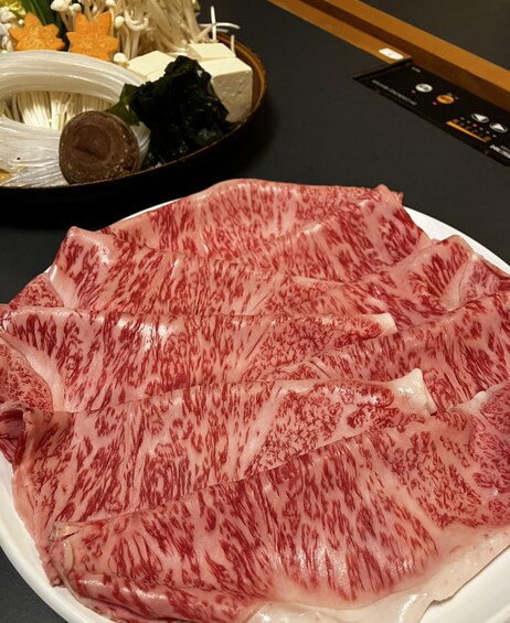 A plate of raw meat with marbling, a bowl of mushrooms, and some leafy greens. 4