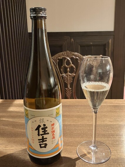 A bottle of sake with a label and a glass of sake beside it on a wooden table. 3
