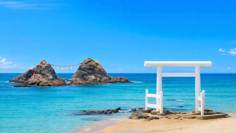 A beach with a white archway and a rope bridge over rocks. 2