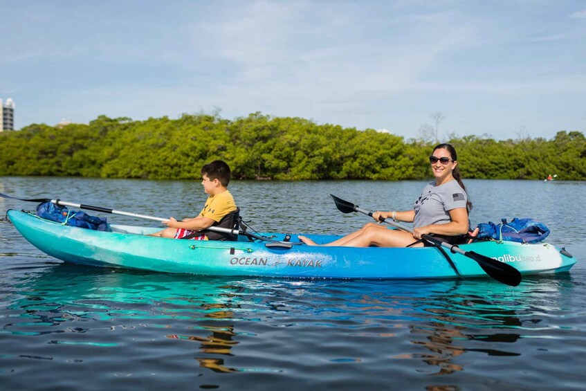 Two people kayaking on a calm body of water with a forested shoreline in the background. 1