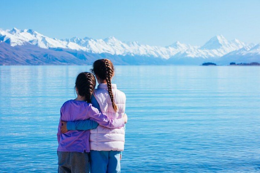 Two people embracing by a calm lake with snow-capped mountains in the background. 4