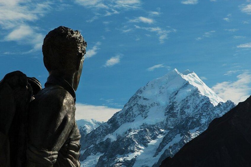A statue of a person with a backpack overlooking a snow-capped mountain. 5