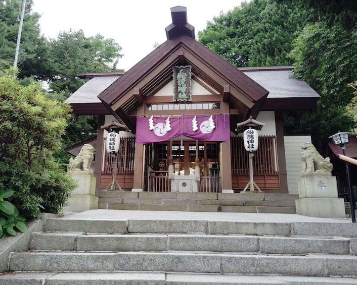 A traditional Japanese shrine with a purple entrance canopy, stone steps, and lion statues. 2