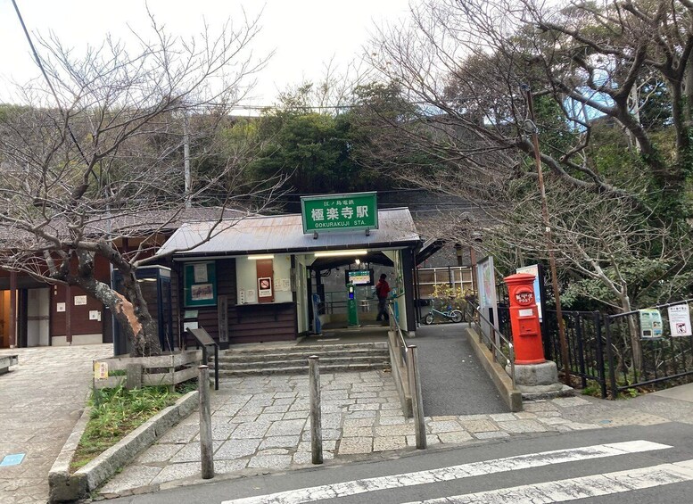A Gokurakuji Station entrance with a green sign, a red post box, and a bicycle parked outside. 3