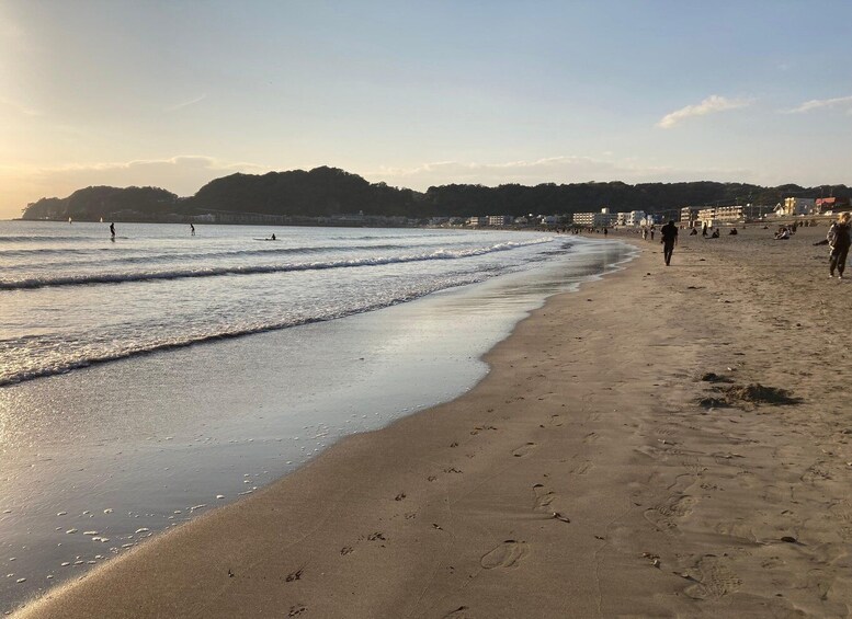 A beach with people walking and a person surfing. 5